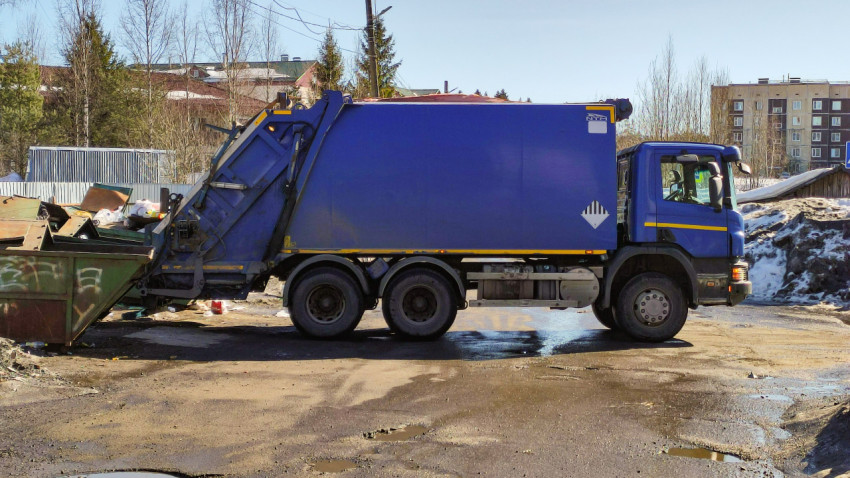 Мусоровоз забирает отходы с контейнерной площадки в городском районе солнечным днем
