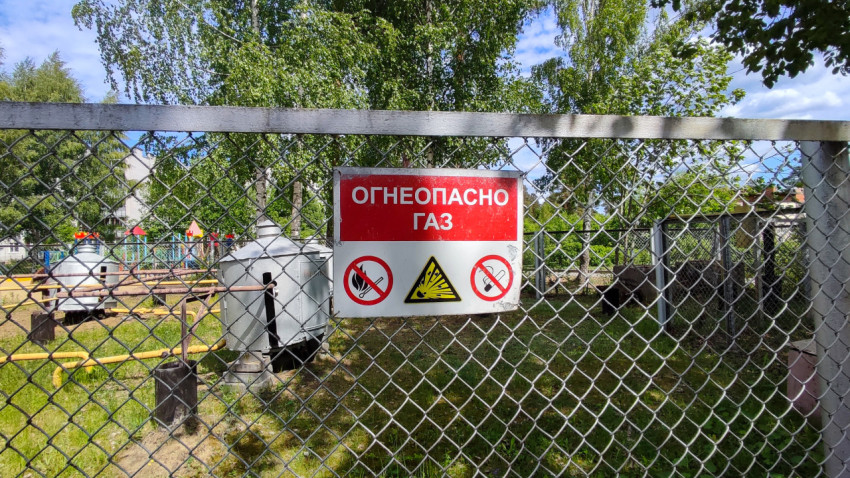 Предупредительный знак «Огнеопасно газ» на фоне деревьев и жилых домов
