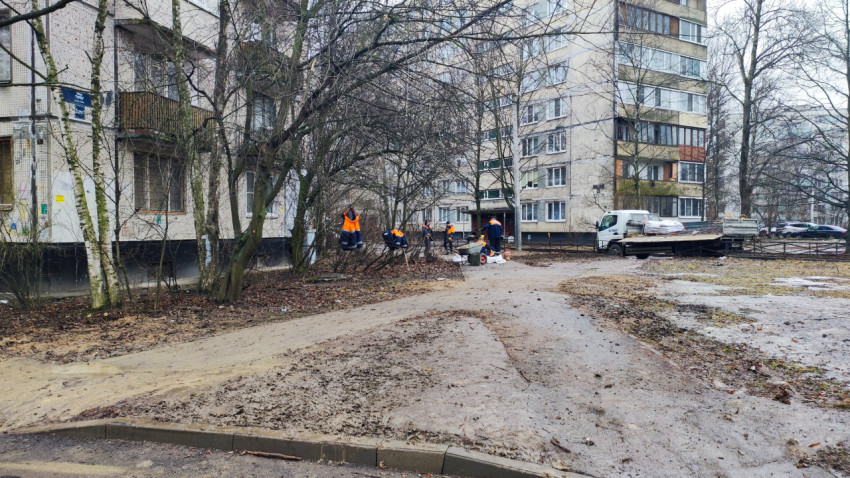 Рабочие в оранжевых жилетах убирают территорию во дворе