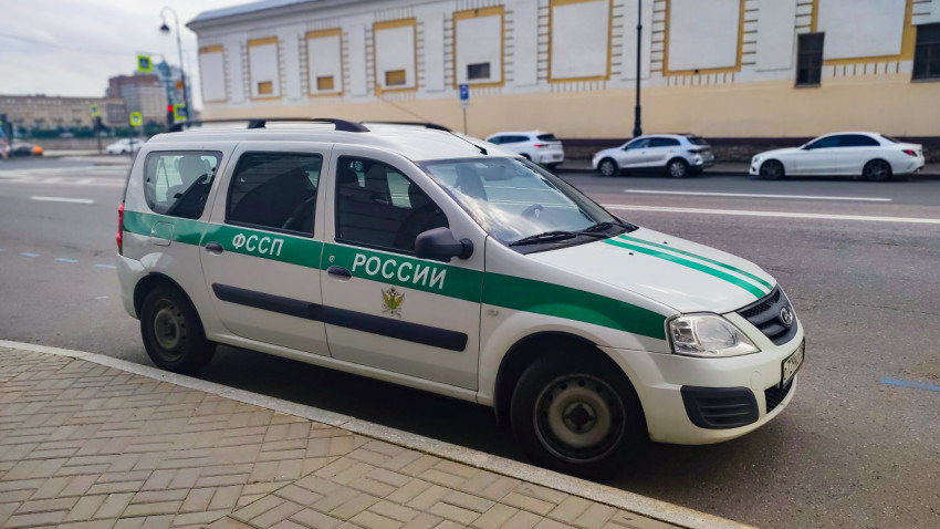Служебный автомобиль ФССП России с зелёной полосой, припаркованный у тротуара