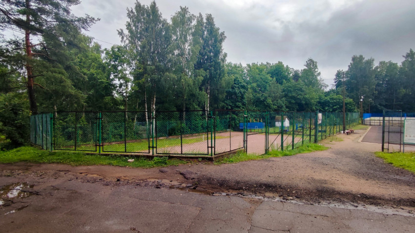 Панорама спортивных площадок с ограждением и мокрой дорожкой после дождя
