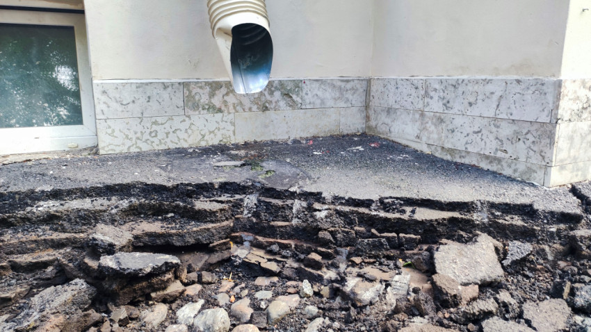 Разрушенное асфальтовое покрытие у цоколя здания под водосточной трубой