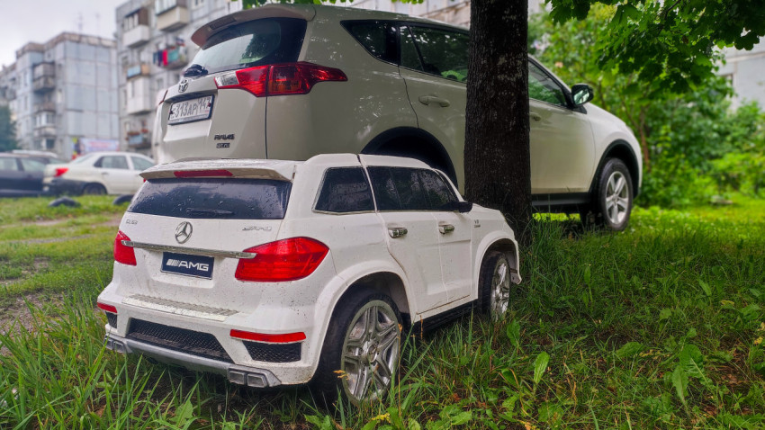 Крупный план детского электромобиля AMG на фоне Toyota RAV4 у дерева