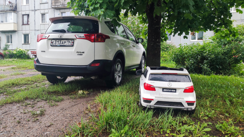 Toyota RAV4 рядом с детским электромобилем Mercedes AMG на сырой дворовой площадке