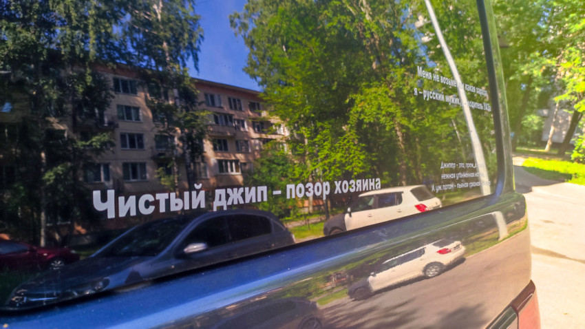 Наклейка «Чистый джип — позор хозяина» на заднем стекле автомобиля с отражением двора