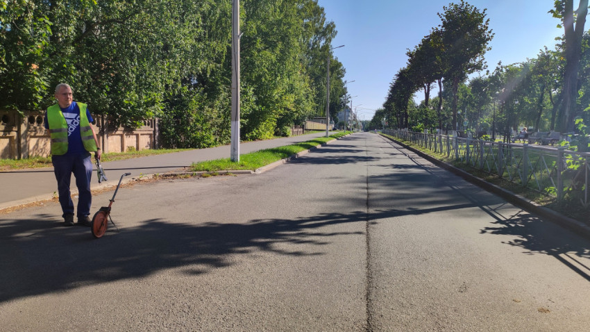 Дорожный рабочий в сигнальном жилете и измерительное колесо на асфальте у края улицы