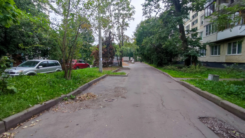 Дворовый проезд с припаркованными автомобилями и изношенным асфальтом у жилых домов