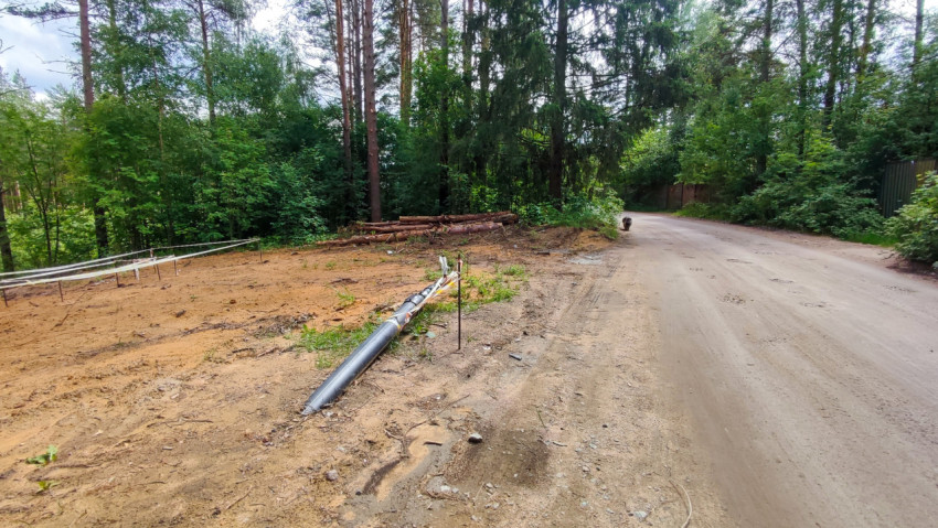 Расчищенная площадка у лесной дороги с уложенной трубой и штабелем брёвен