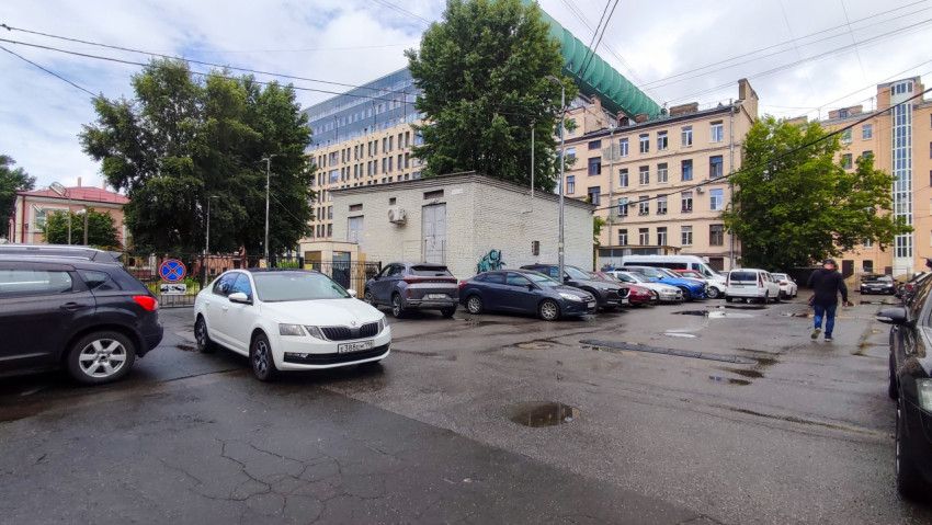 Общий вид двора с автомобилями, лужами и хозяйственным корпусом среди деревьев