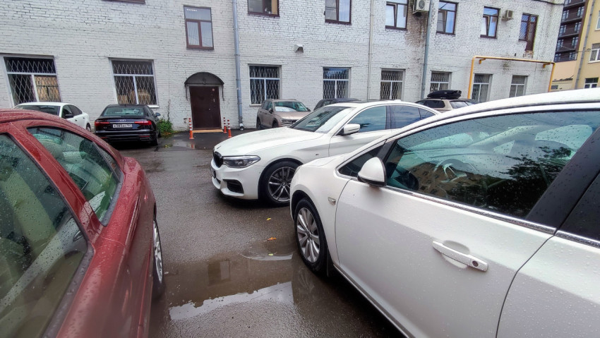 Тесная парковка у белого кирпичного дома с каплями дождя на автомобилях