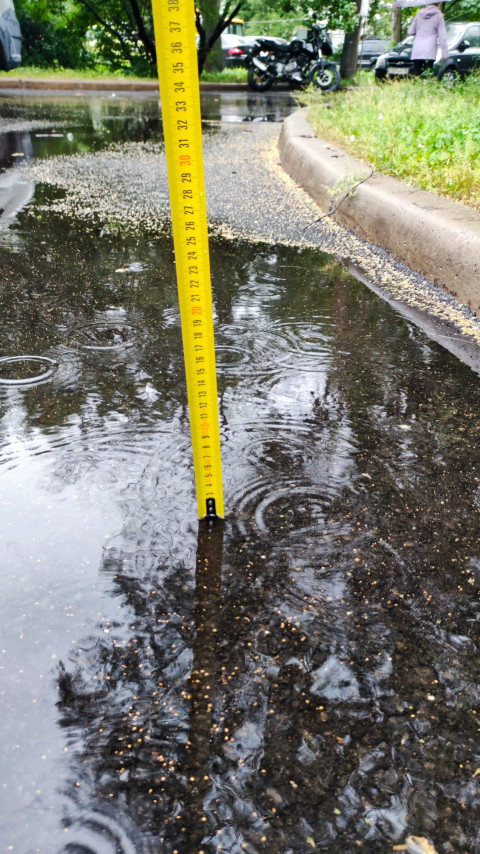 Рулетка в воде у края проезда фиксирует глубину лужи во время дождя